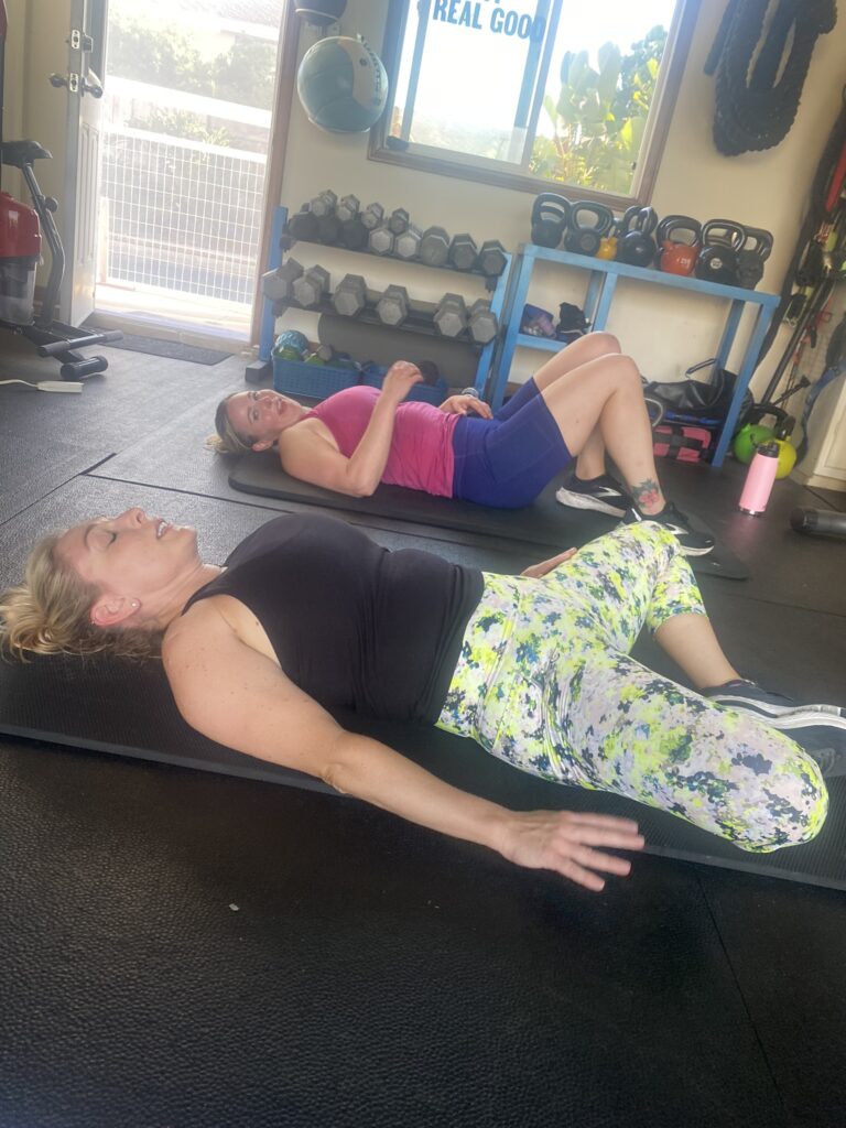 Women in their 30s and 40s lying on mats during post-workout recovery in a strength training studio