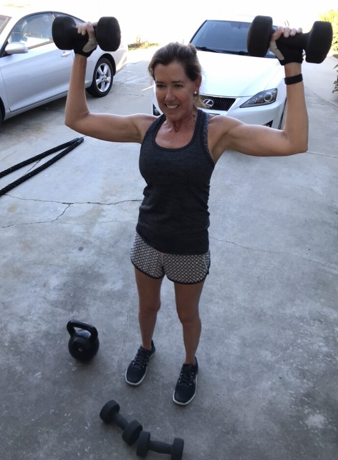 Client posing with dumbbells in front of the Lynn Montoya Fitness sign after a strength training session