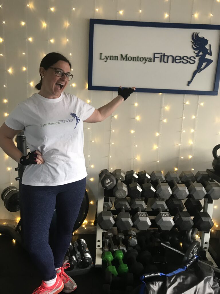 Client posing with dumbbells in front of the Lynn Montoya Fitness sign after a strength training session