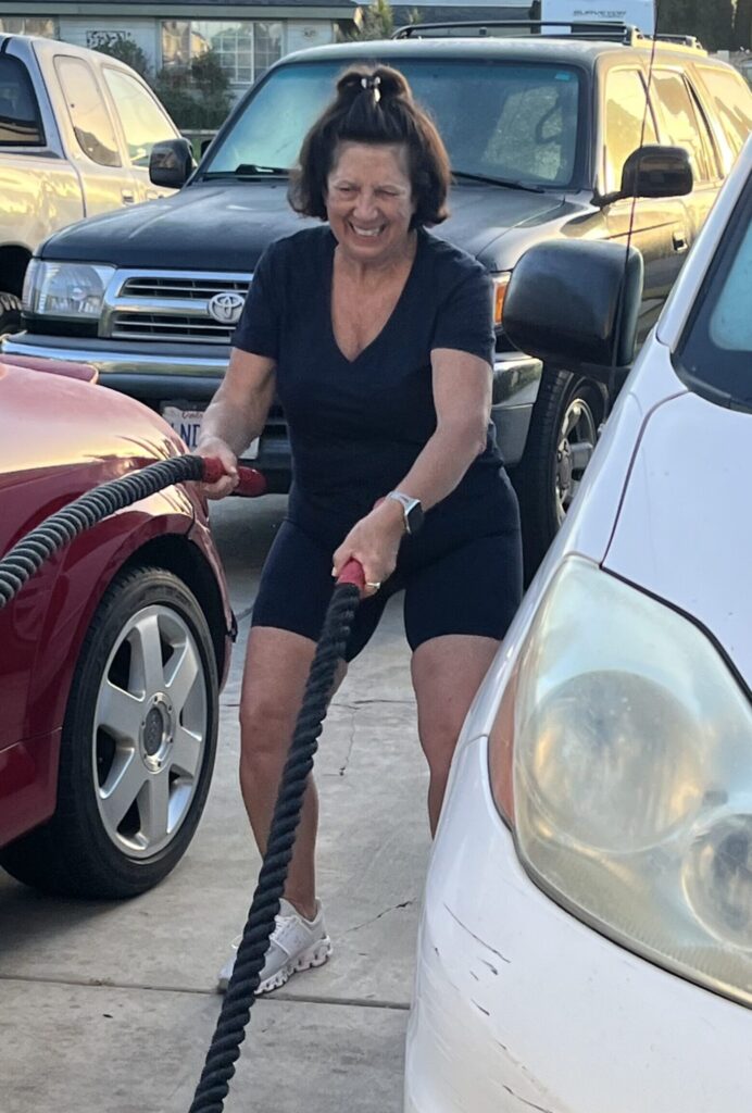 Midlife woman smiling while using battle ropes during an outdoor workout
